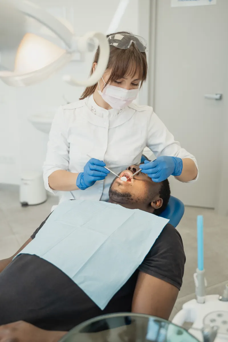 A dentist in a white coat looks at a man's teeth in the dental chair
