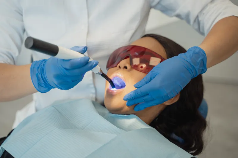 A dentist shines a small blue light on a patient's tooth to harden a filling