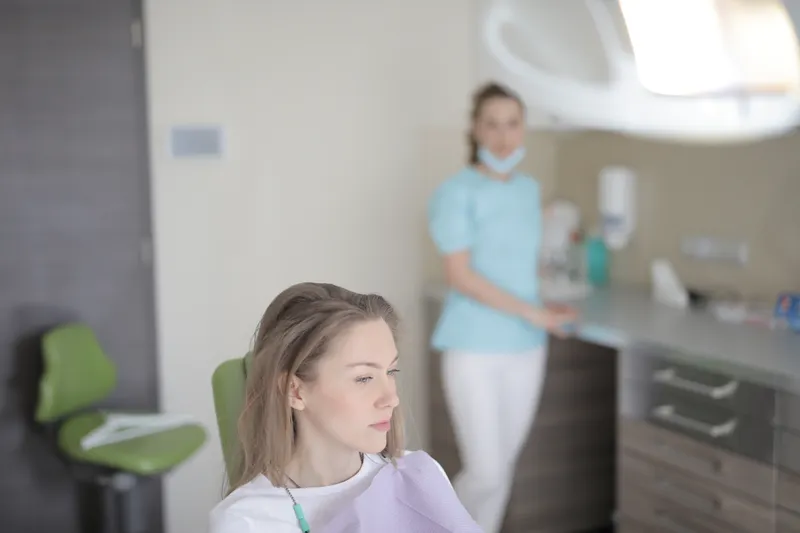 A young woman sits in a dental chair, waiting calmly, with the dental team in the background