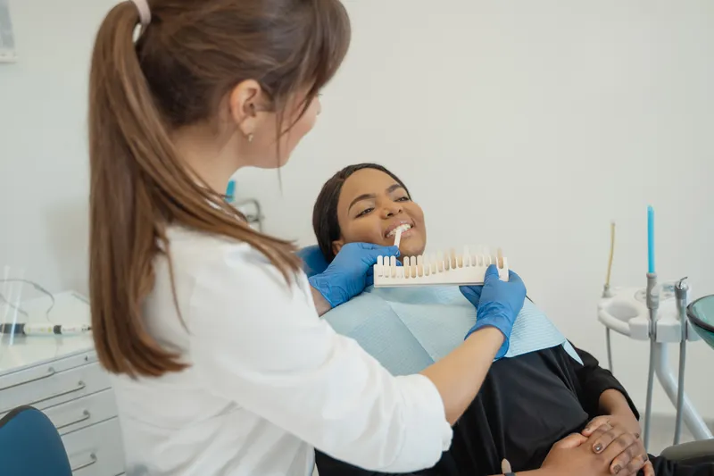 A dentist holds a tooth colour guide up to a smiling patient's teeth
